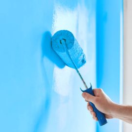 Male hand painting wall with paint roller. Painting apartment, renovating with blue color paint